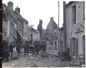 American troops move forward amidst debris in a French town